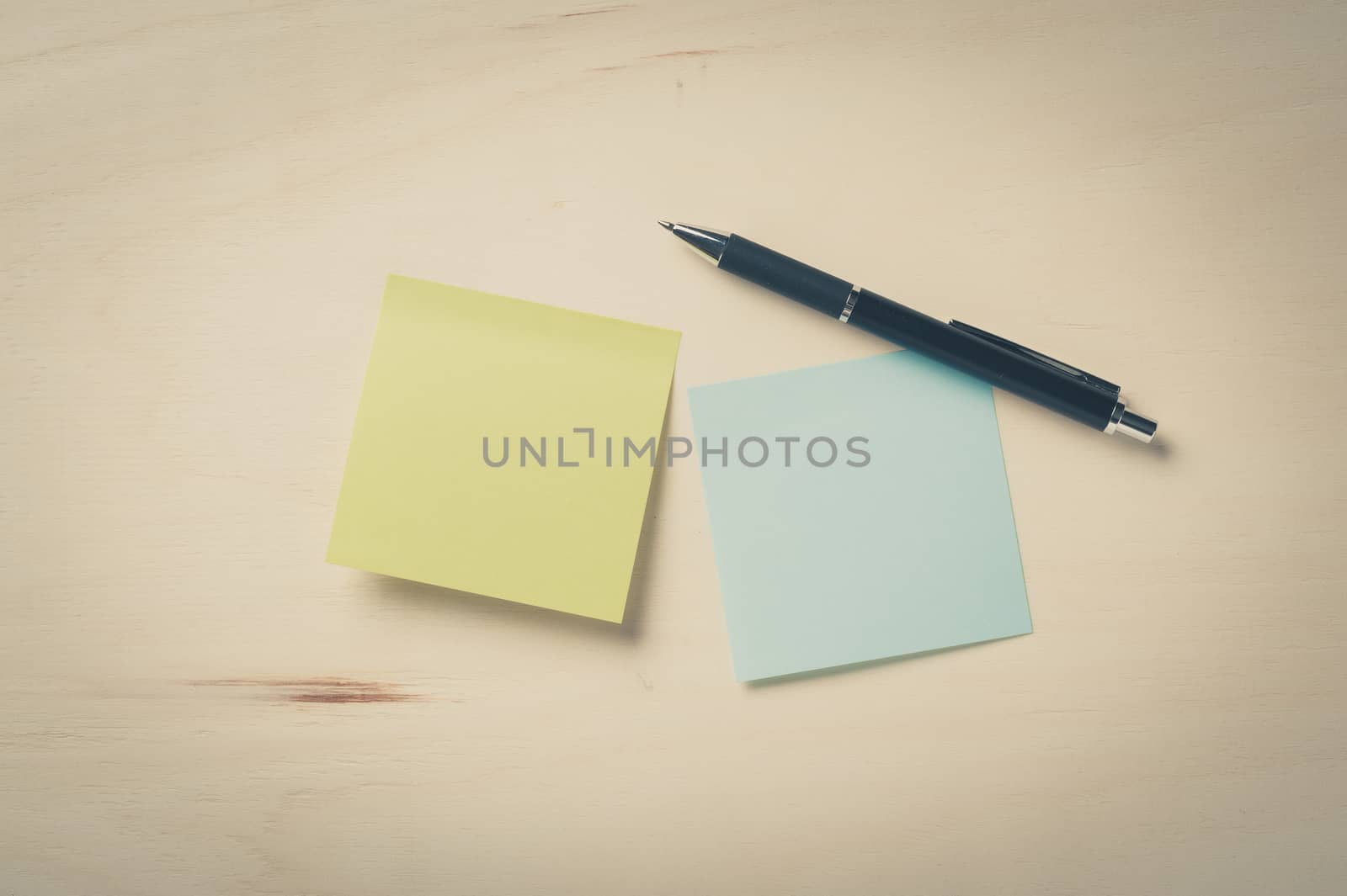 Sticky paper including blue, and green color with blank area for text or message stick on wood table with pen in morning time with vintage filter effect