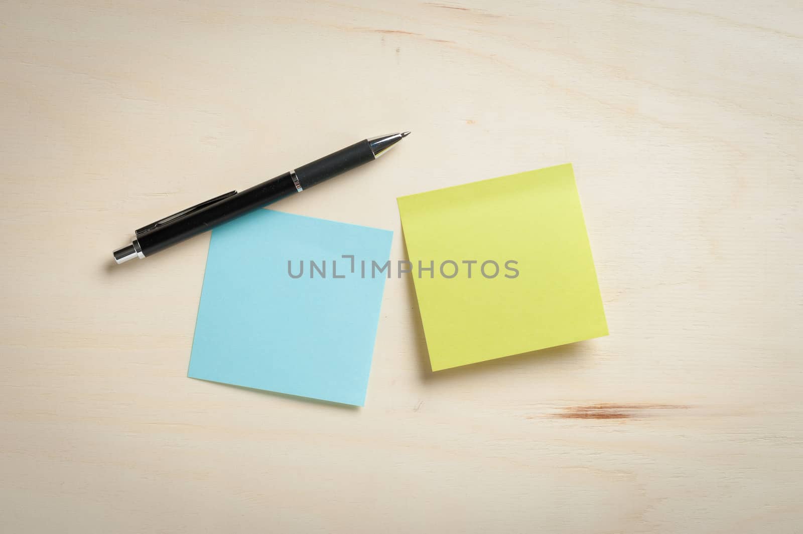 Sticky paper including blue, and green color with blank area for text or message stick on wood table with pen in morning time