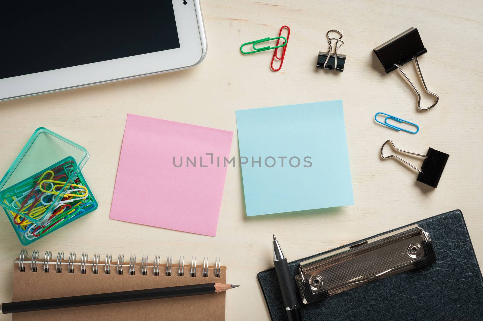 Sticky paper including blue, and green color with blank area for text or message stick on wood table with office supplies and small tablet pc