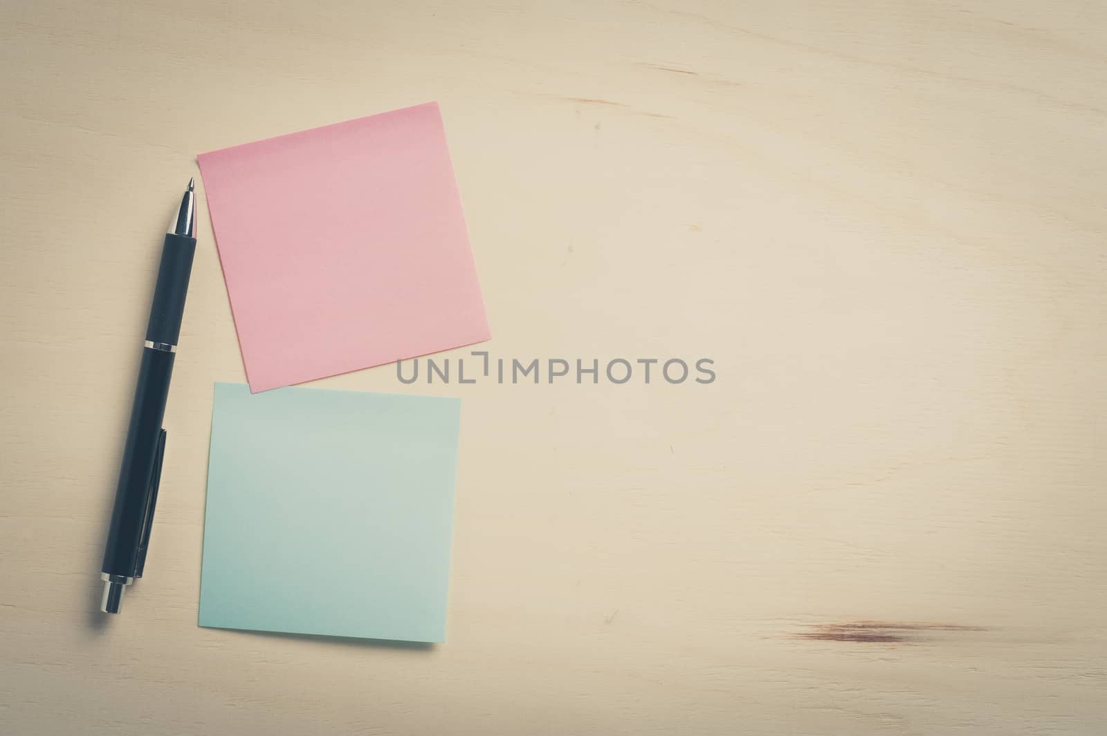 Sticky paper including blue, and pink color with blank area for text or message stick on wood table with pen, processed with vintage filter effect