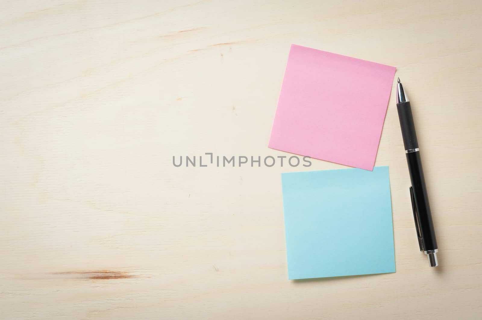 Sticky paper including blue, and pink color with blank area for text or message stick on wood table with pen