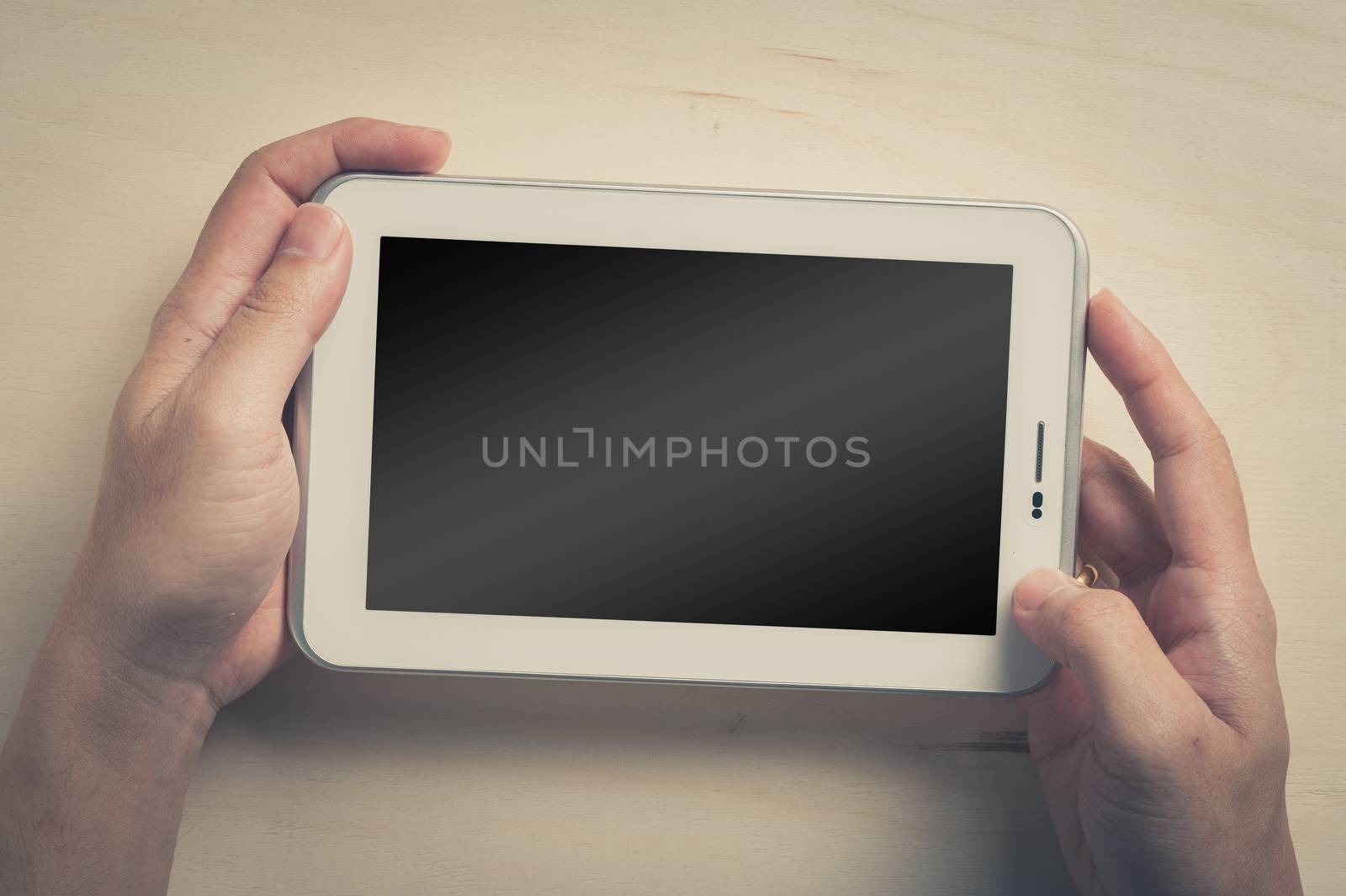 Young man hands holding small tablet with blank area on touchscreen on wood table with vintage filter effect