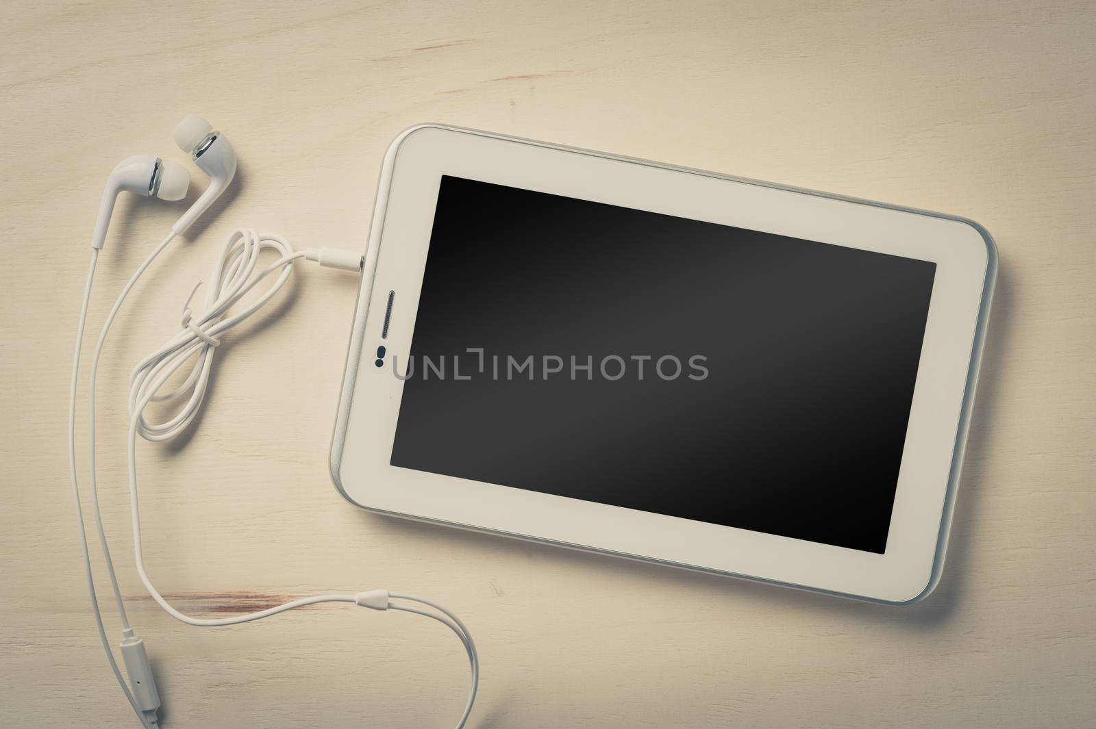 Small tablet pc with blank area on touchscreen and in ear headset on wood table with vintage filter effect
