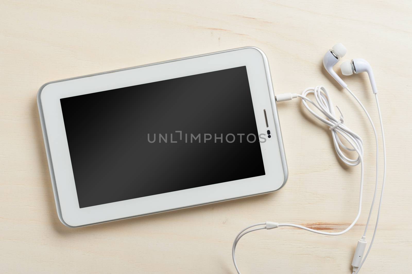 Small tablet pc with blank area on touchscreen and in ear headset on wood table
