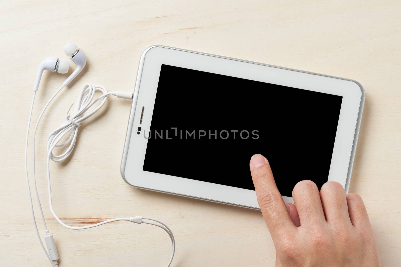 Young man hand touching on small tablet pc screen on wood table with in ear headset beside