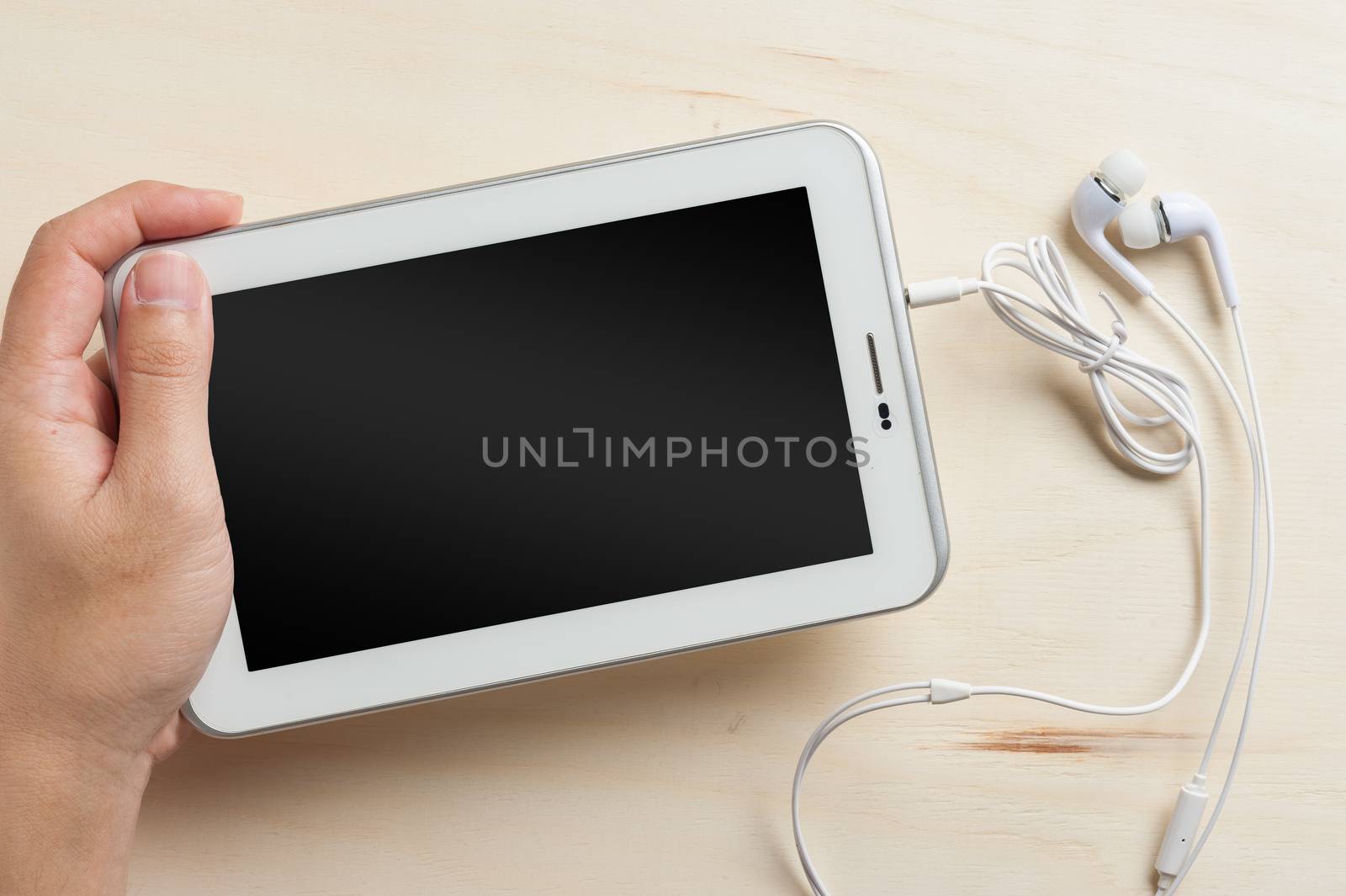 Young man left hand holding small tablet pc screen on wood table with in ear headset beside