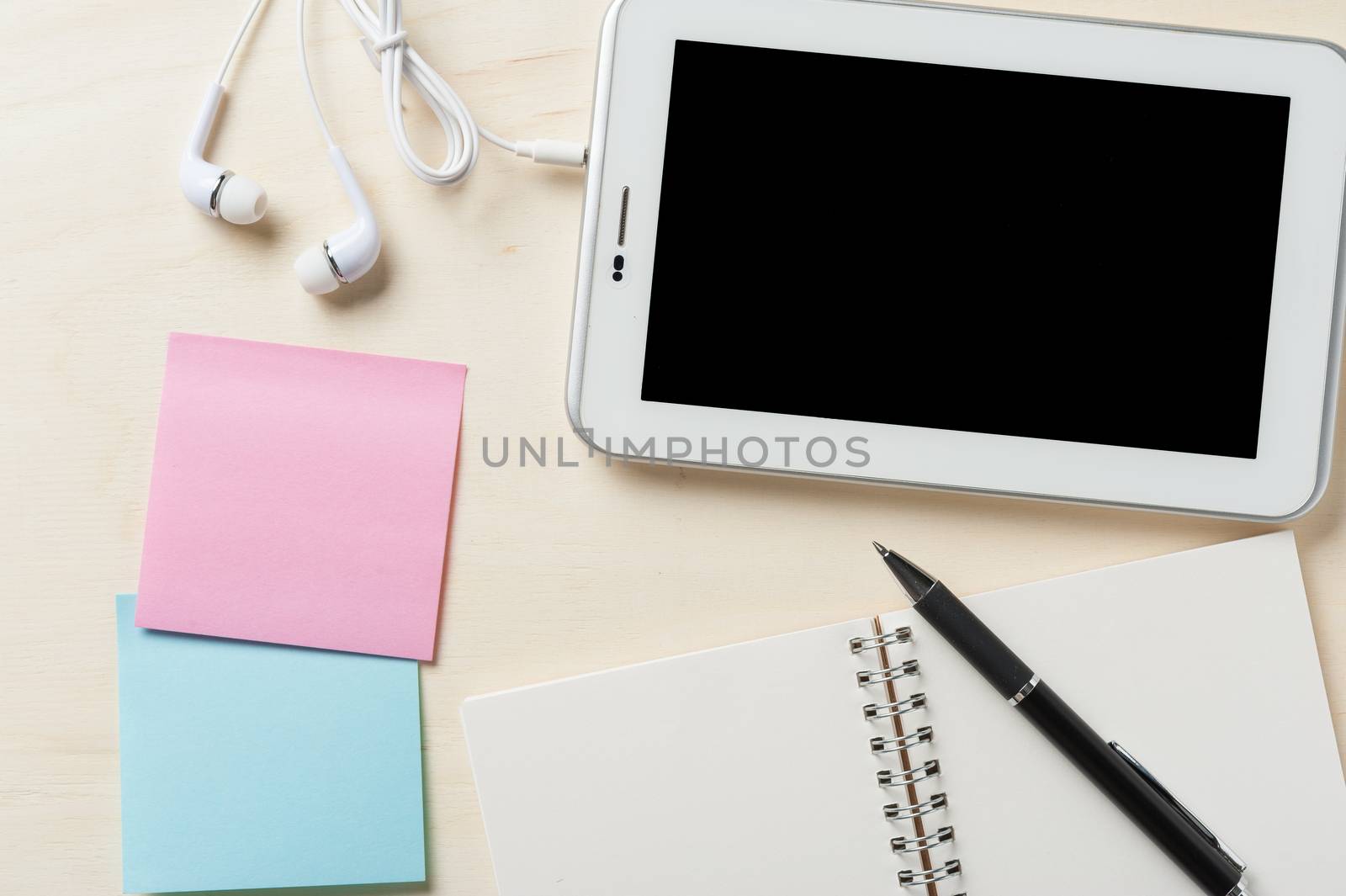 Small tablet pc with blank area on touchscreen, in ear headset, notebook, sticky paper, and pen on wood table