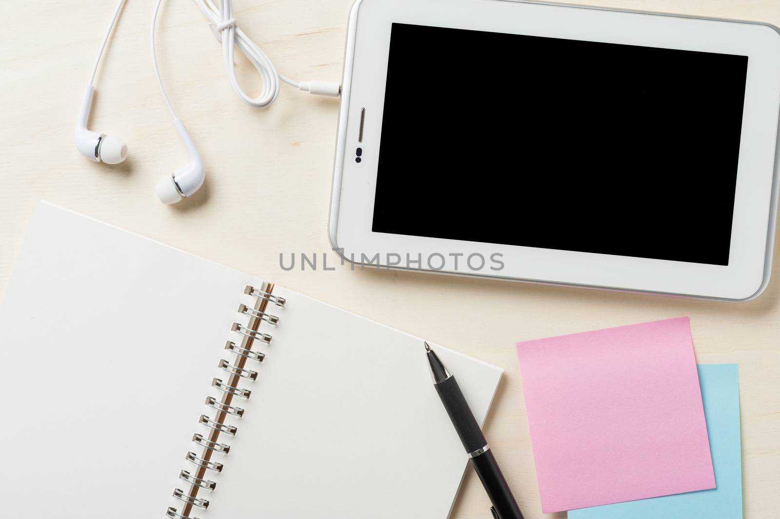 Small tablet pc with blank area on touchscreen, in ear headset, notebook, sticky paper, and pen on wood table