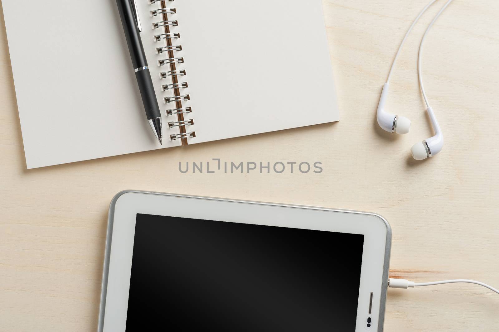 Notebook, pen, small tablet pc, and in ear headset on wood table
