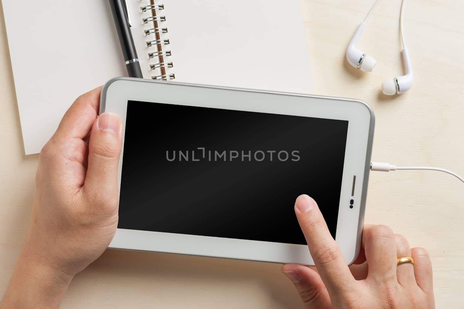 Young man right hand touching on small tablet pc screen on wood table with in ear headset and notebook beside