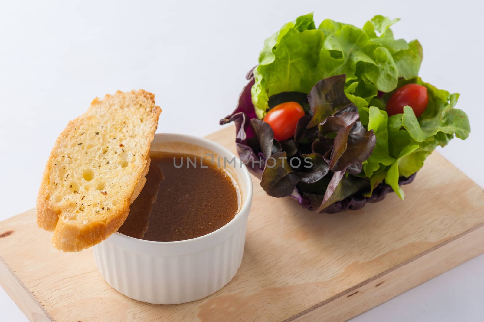 Onion soup in ceramic cup with toast and freash vegetables on wood plate. Clean and healthy eating concept food.