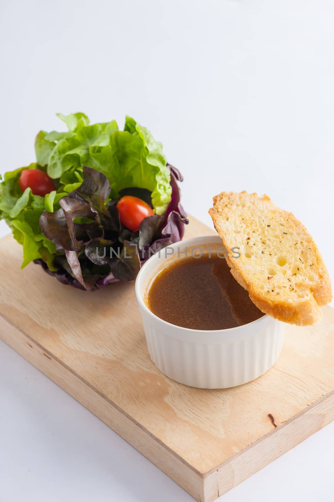 Onion soup in ceramic cup with toast and freash vegetables on wood plate. Clean and healthy eating concept food.