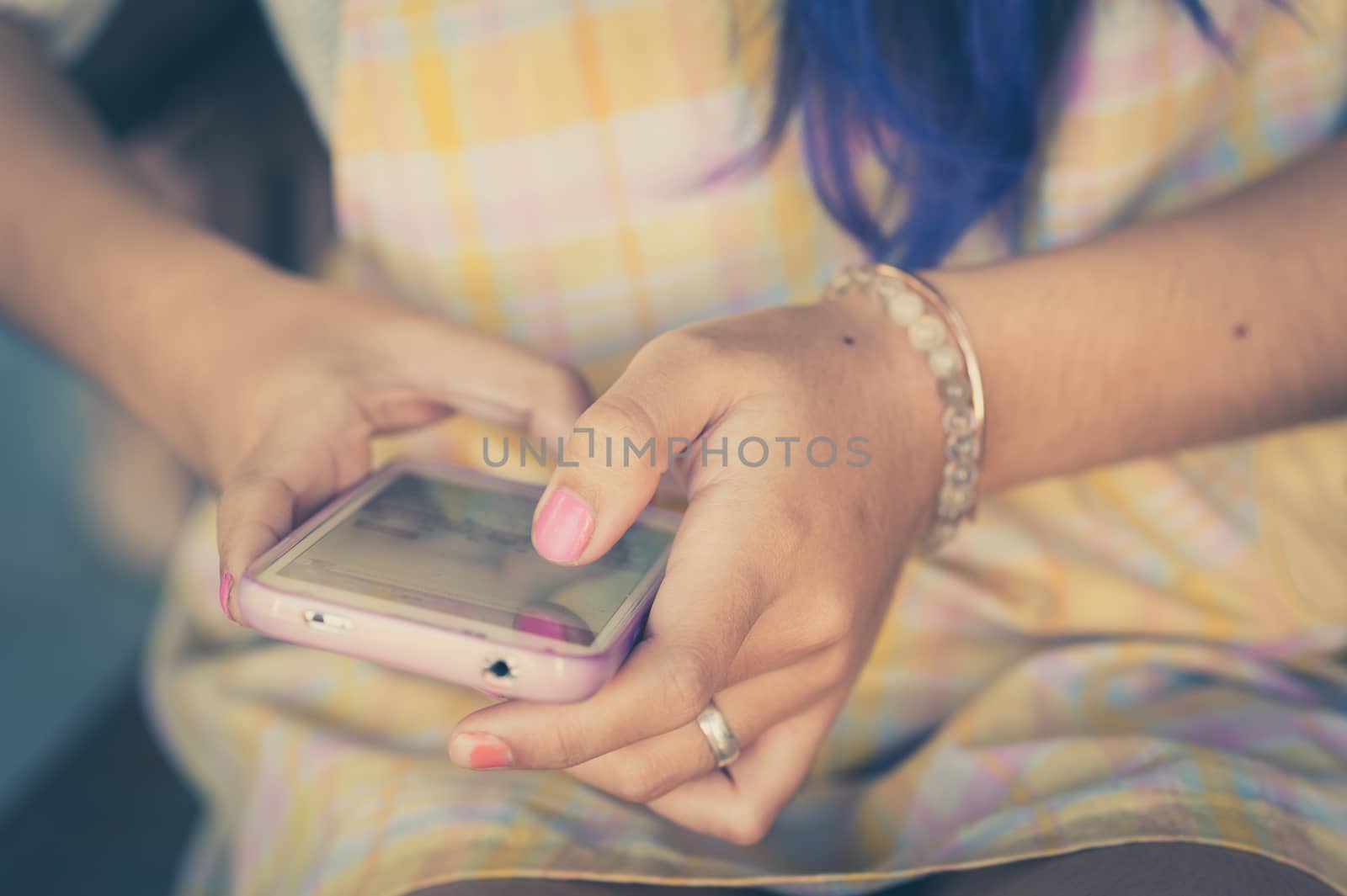 Young hipster woman using smartphone while sitting on wood bench in morning time with vintage filter effect