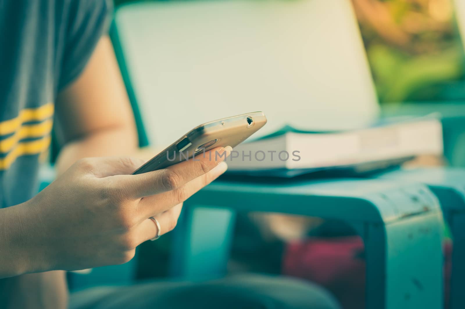 Young woman using smartphone while sitting on wood bench in morning time with vintage filter effect
