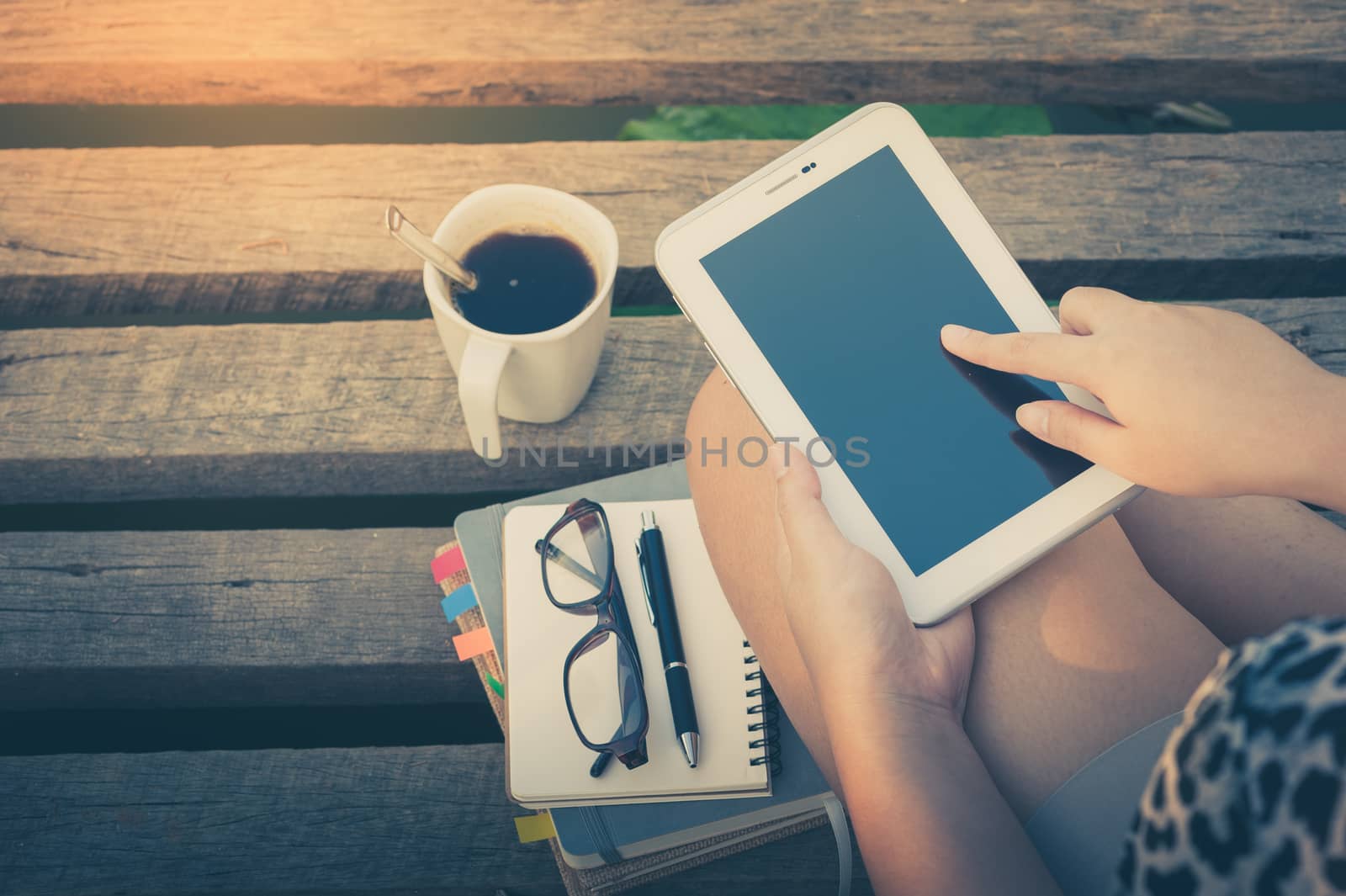 Young woman touching on small talet screen while sitting on wood bridge in morning time on weekend with vintage filter effect