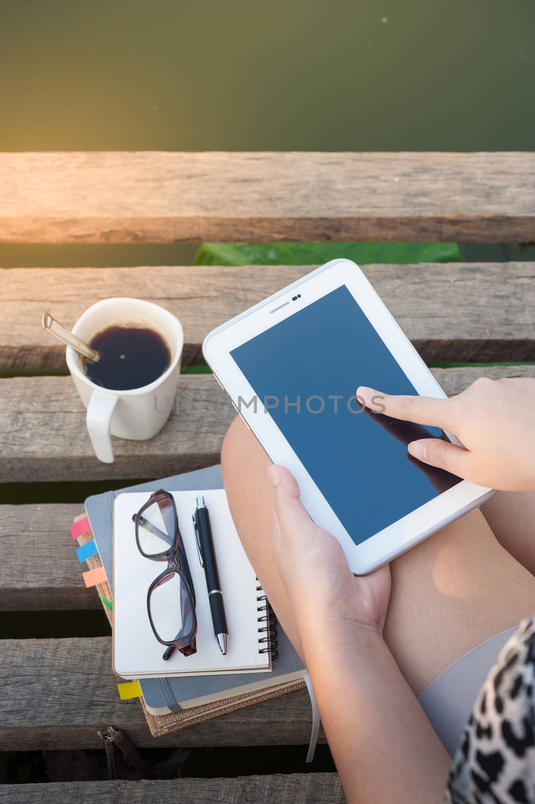Young woman touching on small talet screen while sitting on wood bridge in morning time on weekend