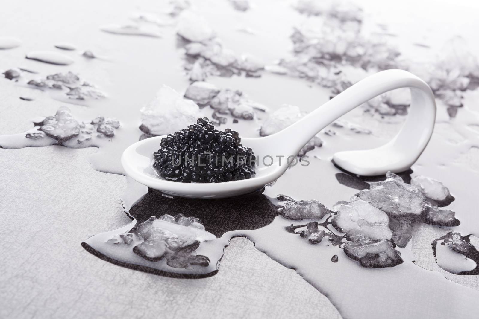 Black caviar on white spoon on ice. Luxurious culinary delicacy, traditional russian black caviar.