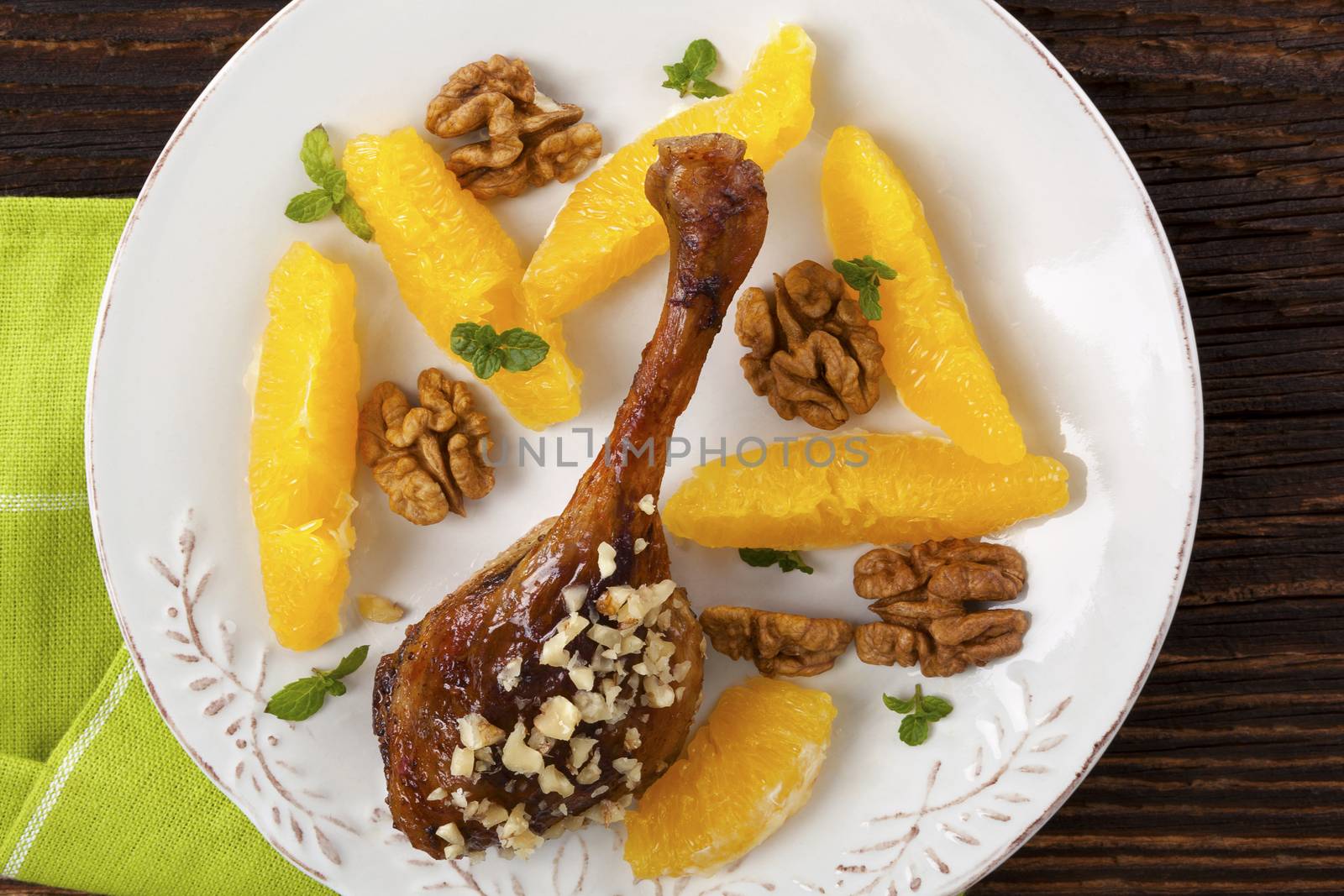 Culinary roast duck with oranges and nuts on plate on wooden table. Flat lay, top view. Delicious festive eating. 