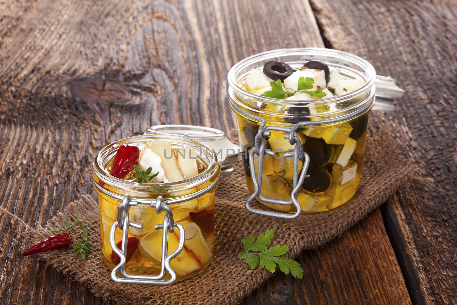 Marinated camembert and greek feat cheese in oil in glass jar on wooden table. Traditional culinary cheese eating. 