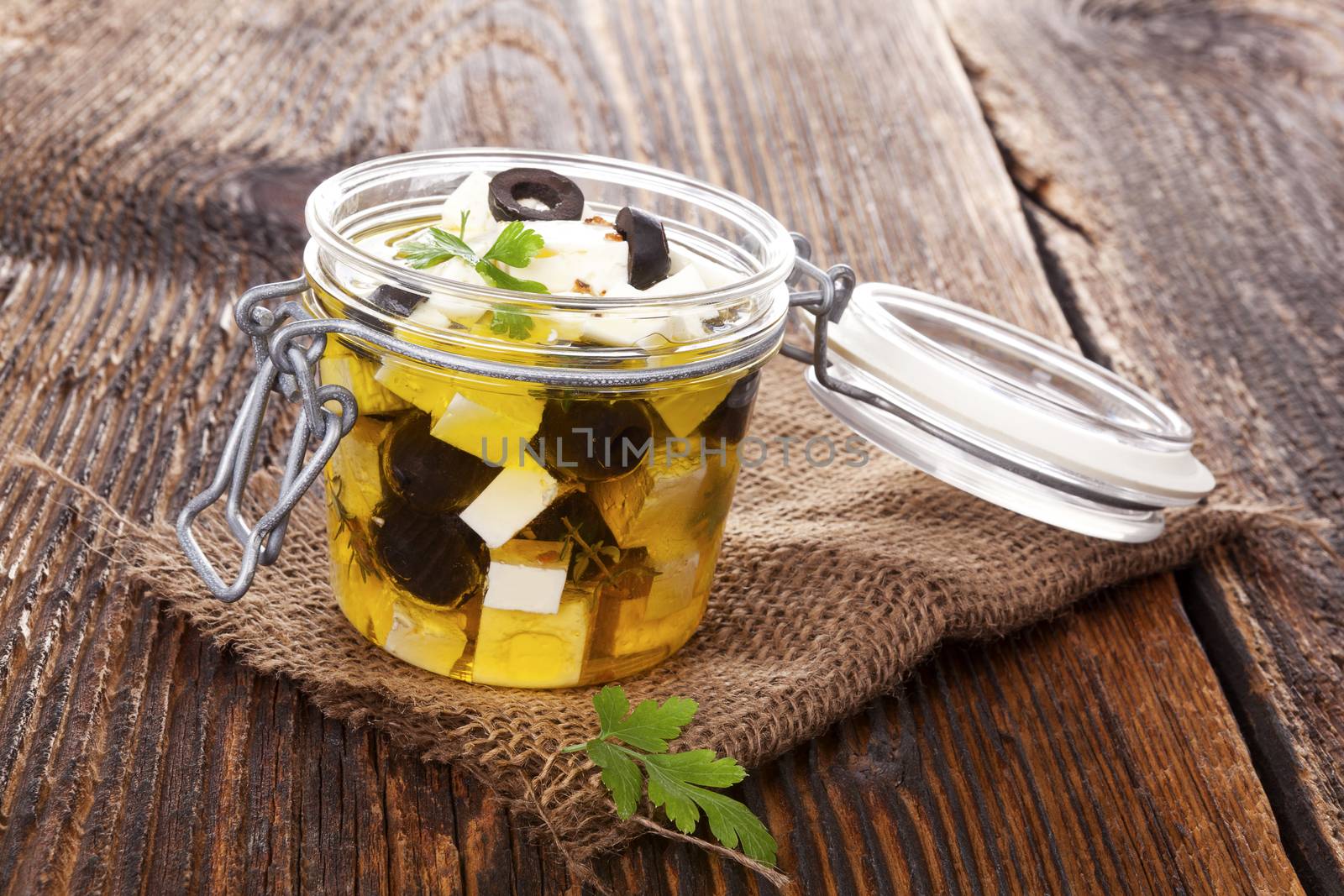 Marinated feta cheese in glass jar on brown wooden background. Culinary marinated cheese, rustic styles.