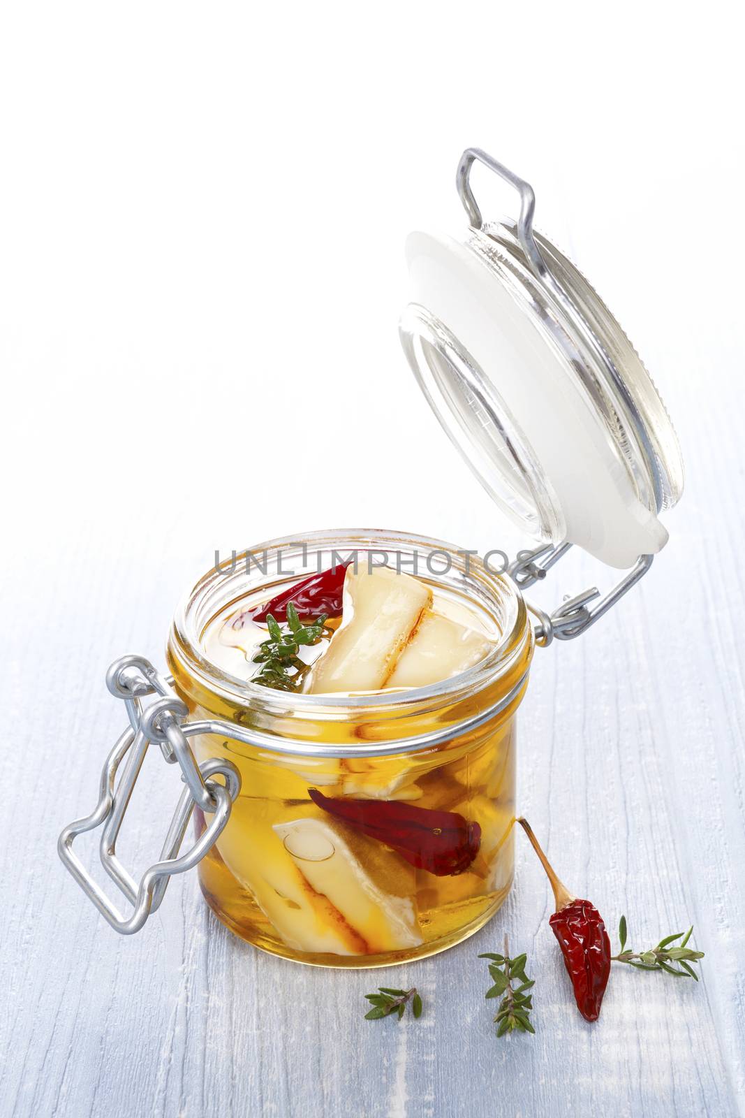 Marinated cheese in glass jar on blue wooden background. Culinary marinated cheese, rustic styles.