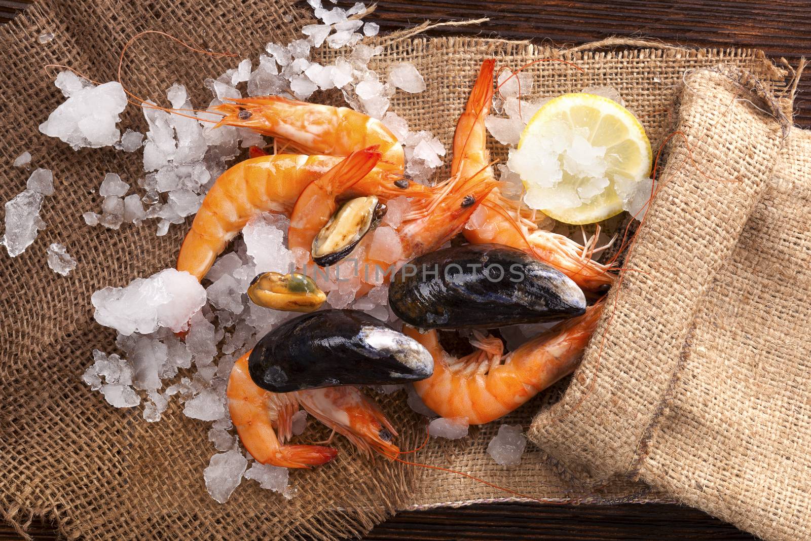 Fresh shrimp with lemon on ice in brown burlap bag on wooden table, top view. Culinary seafood eating.