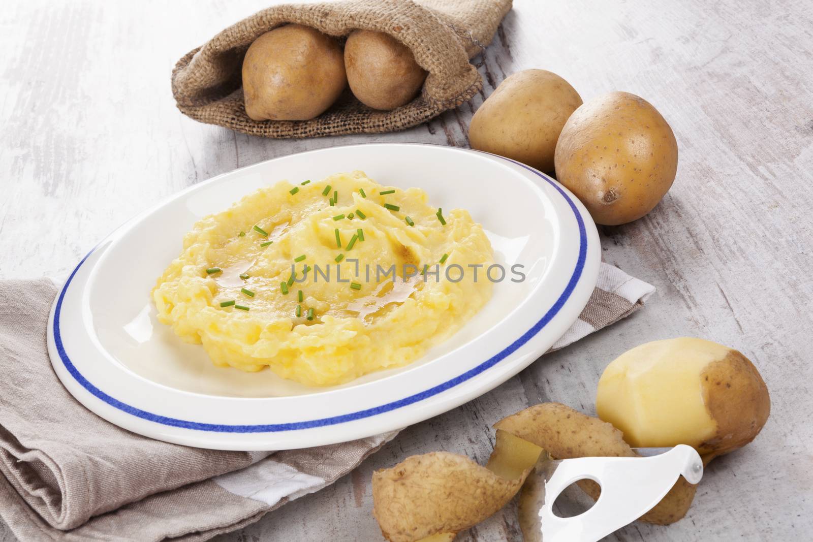 Mashed potatoes on plate, ripe potatoes in burlap bag in background. Culinary potatoe eating. 
