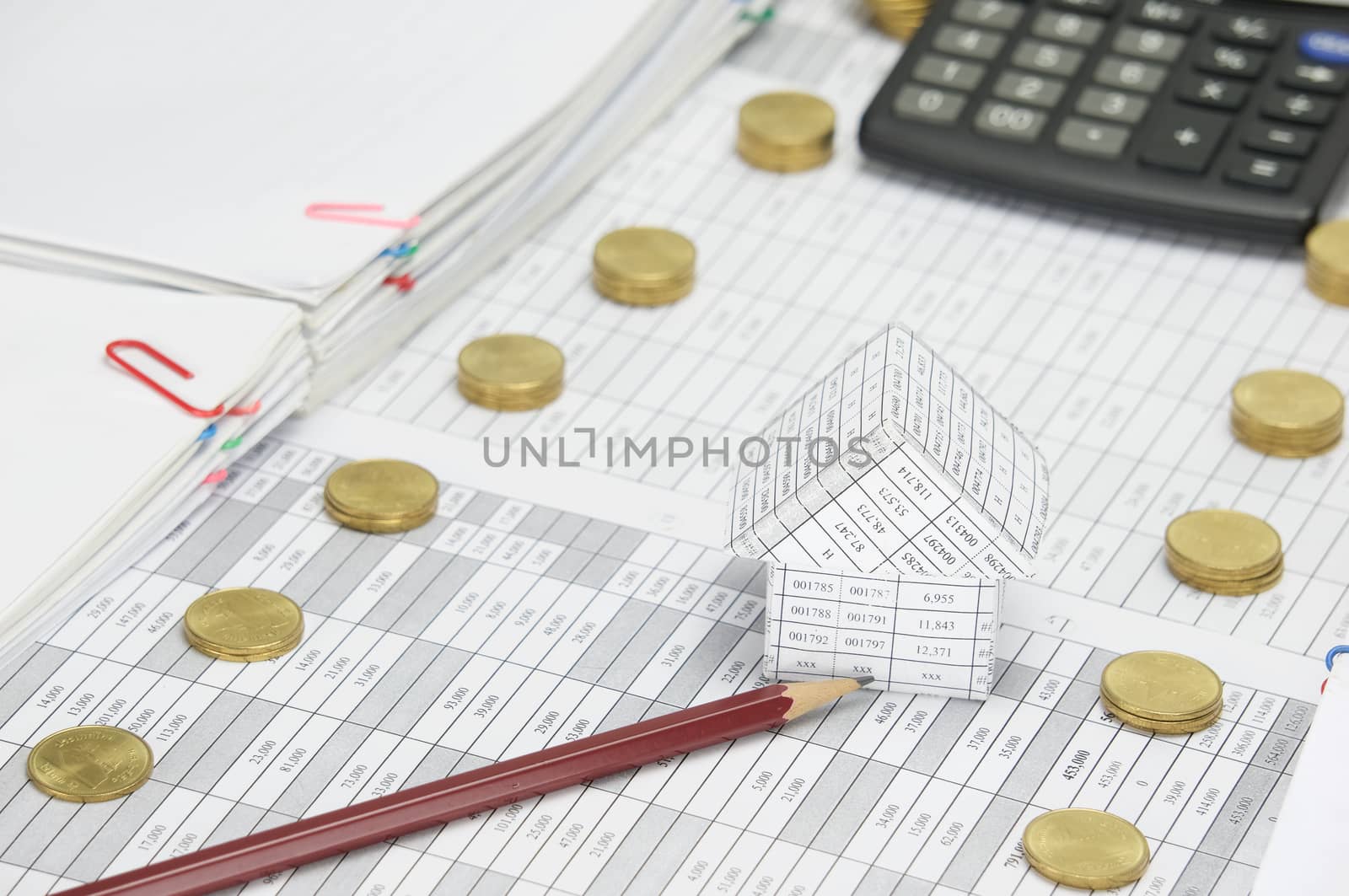 Brown pencil and house on finance account between step pile of gold coins and overload of paperwork with blur calculator as background.