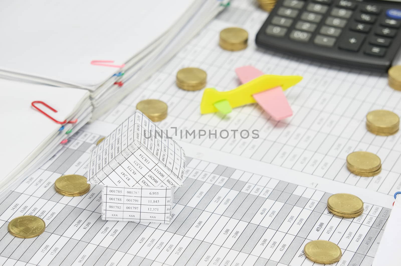 House on finance account between step pile of gold coins and overload of paperwork with blur airplane and calculator as background.