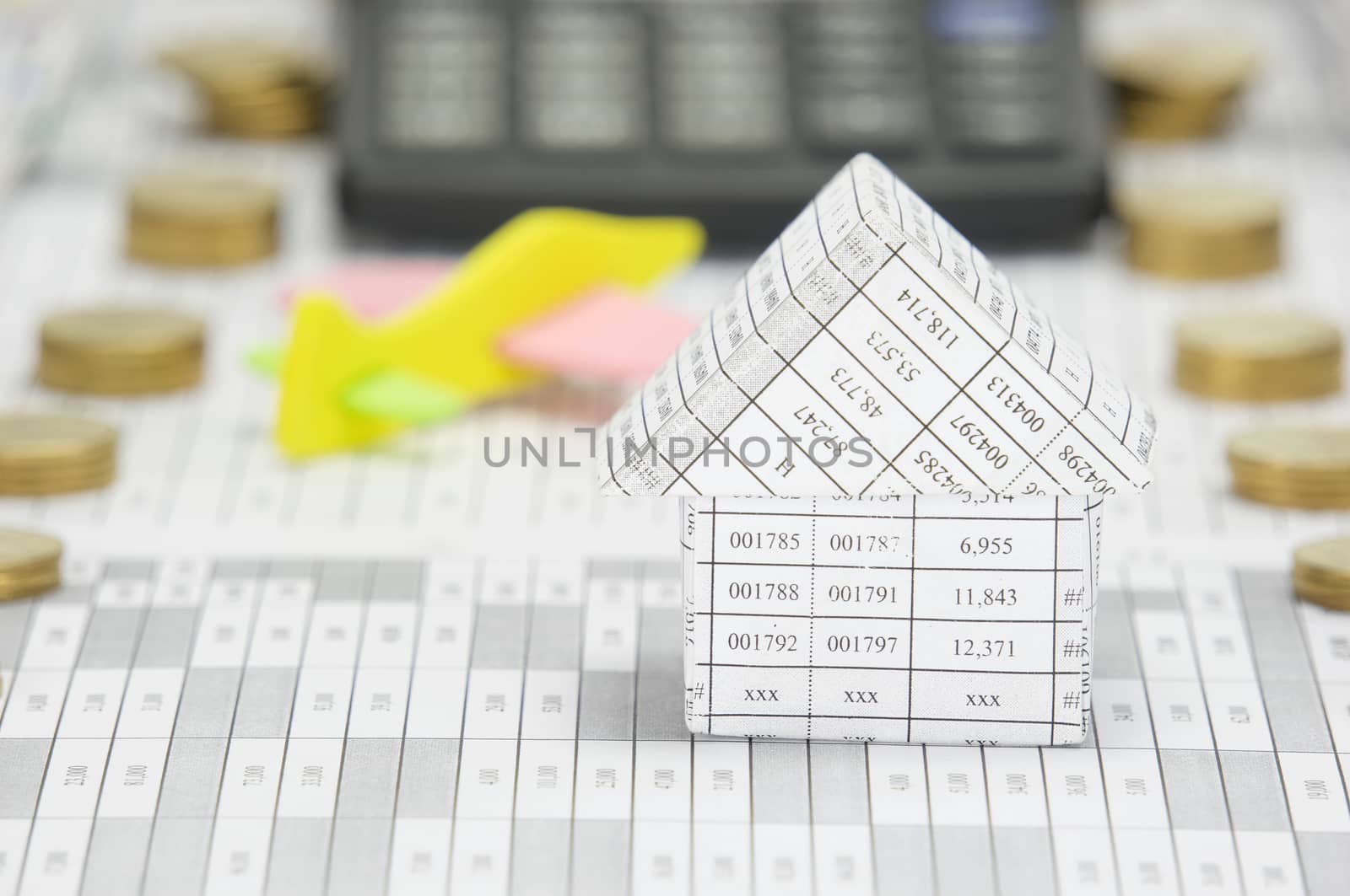 Close up house on finance account between step pile of gold coins and overload of paperwork with blur airplane and calculator as background.