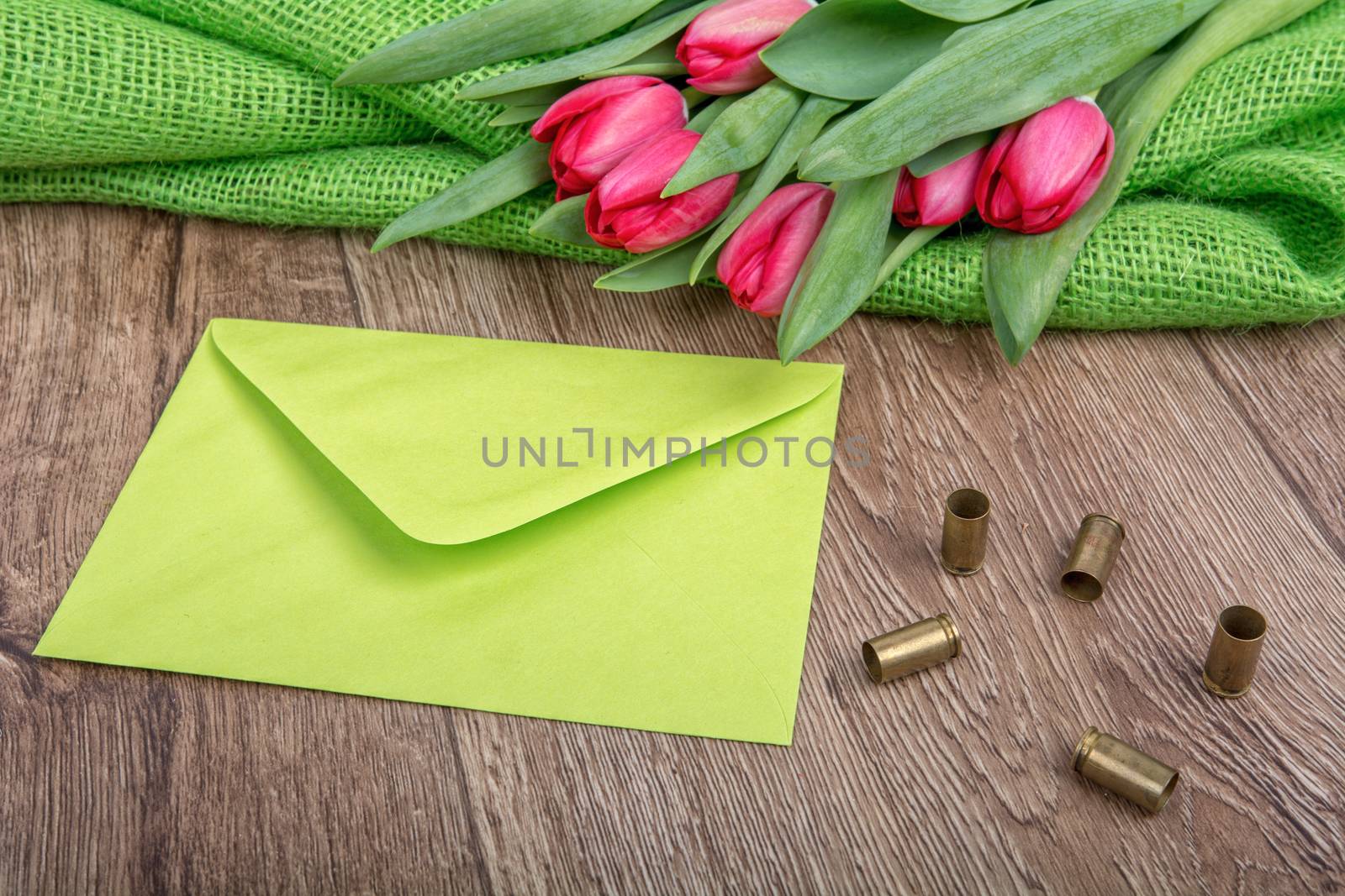 Green envelope, tulips and bullets on a wooden background