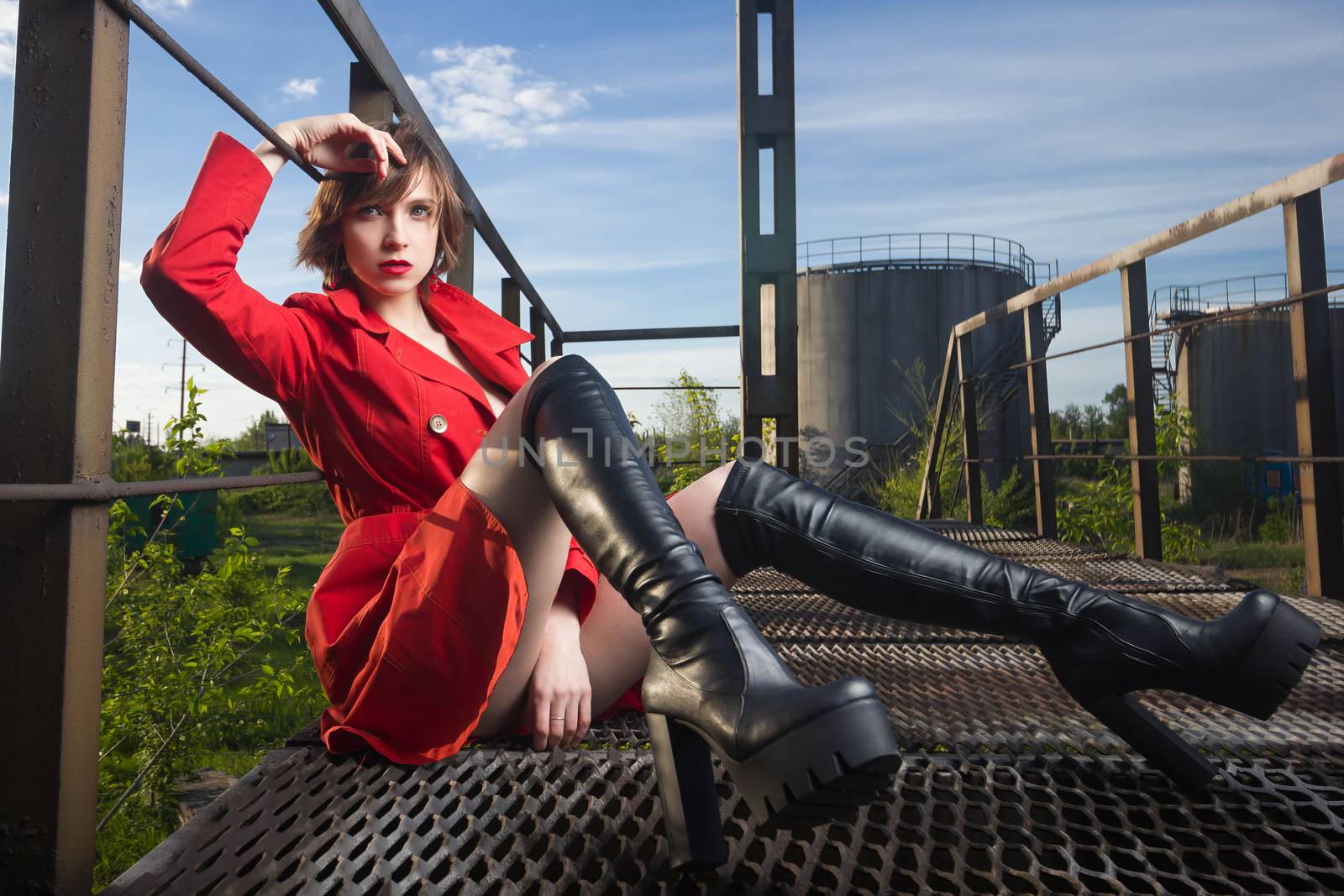 Attractive young woman alluring in sexual lingerie and red coat at grunge industrial setting. Beauty, fashion. Concept: seduction, exhibitionism.