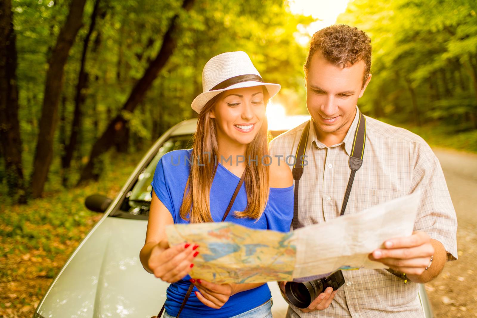 Young travelers standing before a car in the forest, holding map and searching next destination.