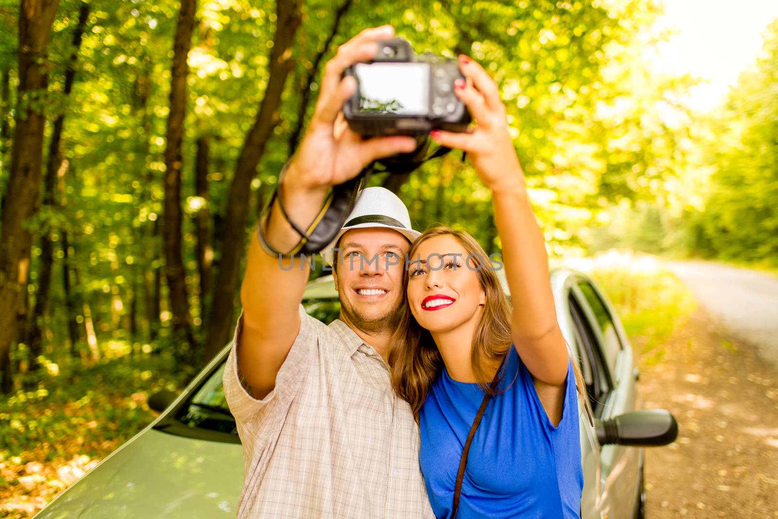 Young travelers standing before a car in the forest and taking photo of themselves.