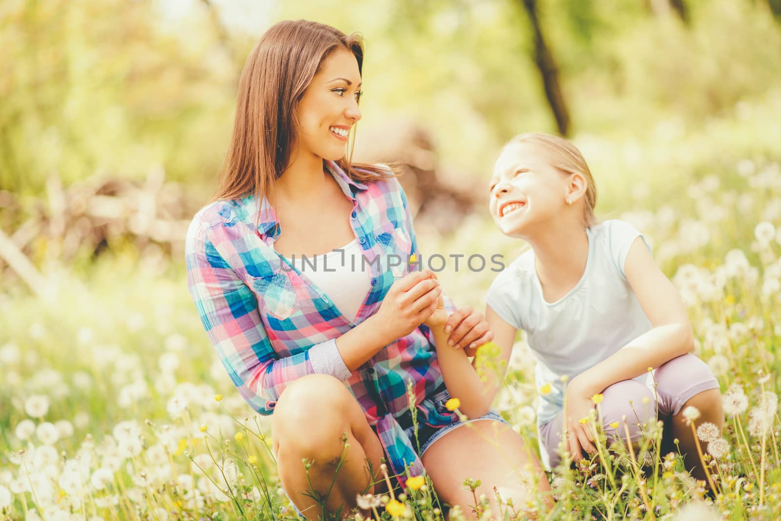 Happy cute little girl blowing dandelion with mother in the park.