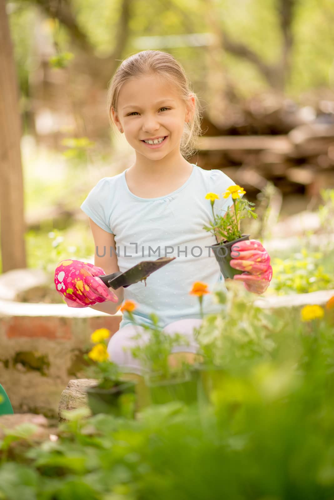 Portrait of a smiling little girl planting flowers in the garden. Looking at camera.