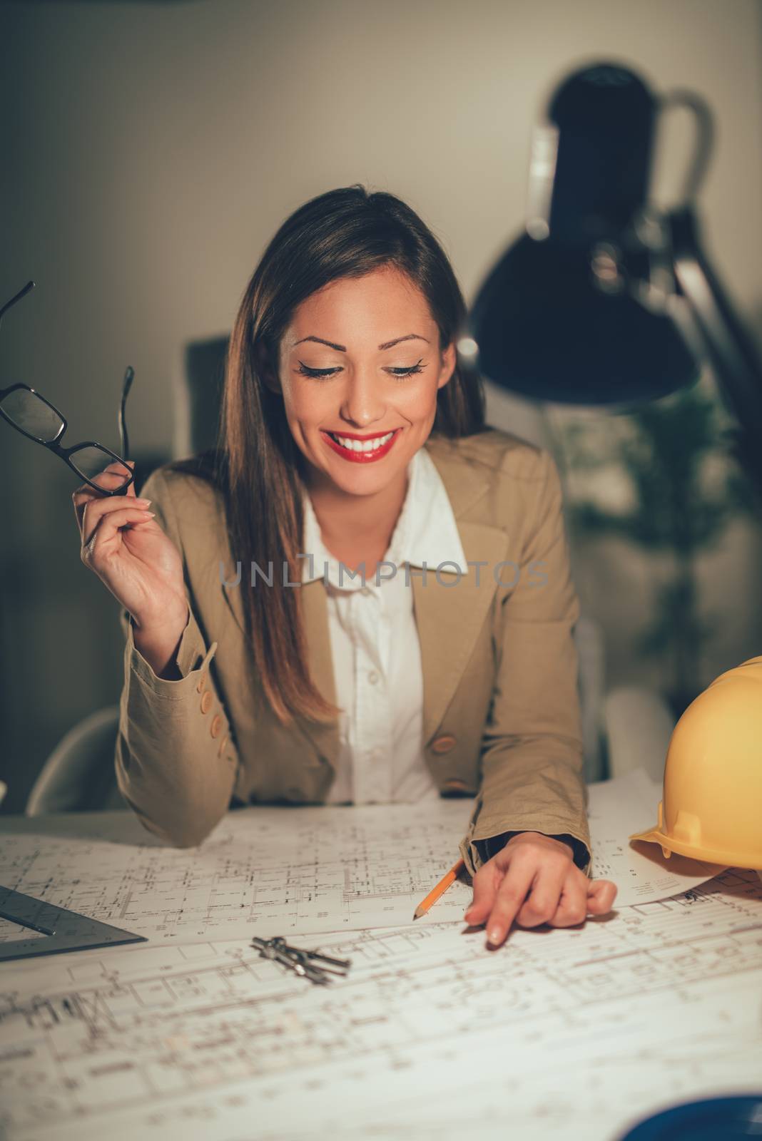 Young smiling female architect analyzing blueprint in the office.