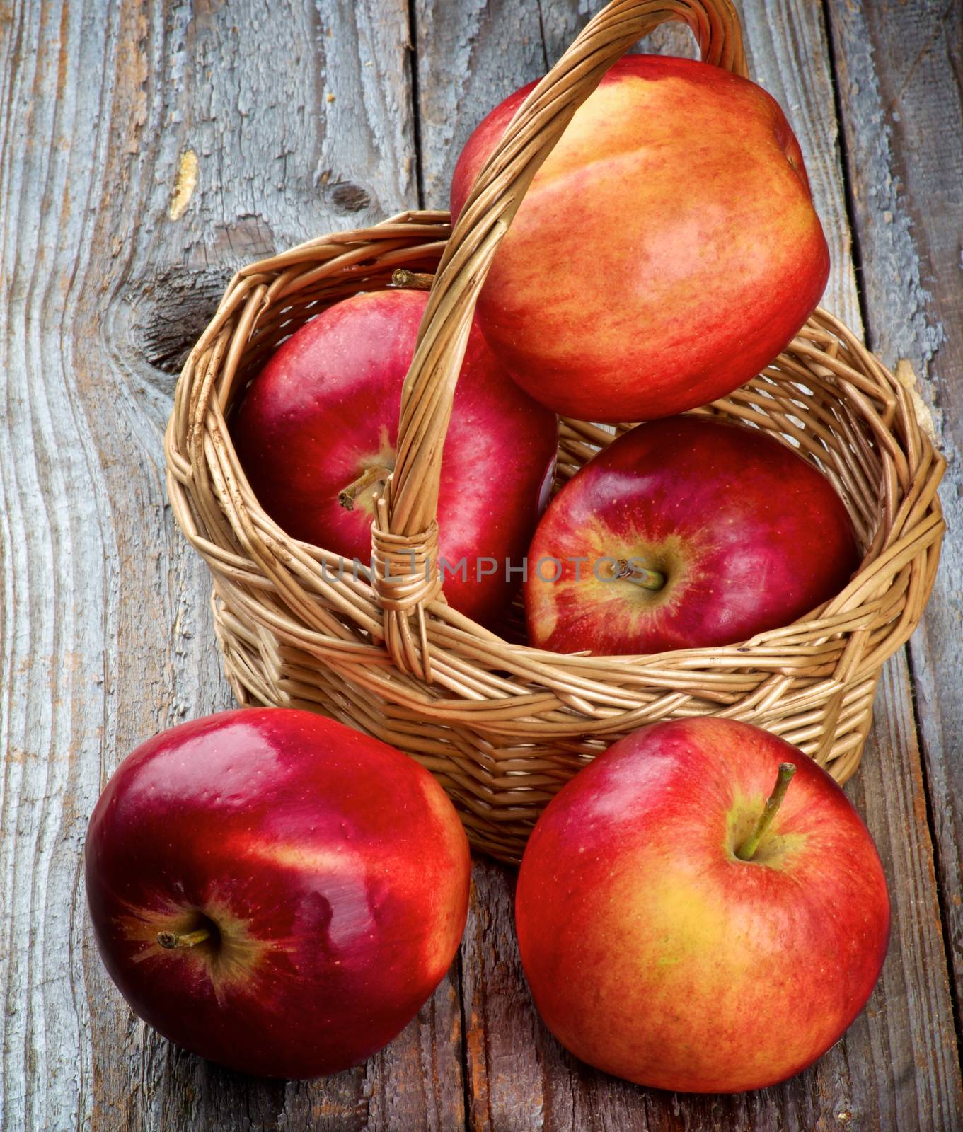 Five Apples Red Delicious in Wicker Basket closeup on Rustic Wooden background