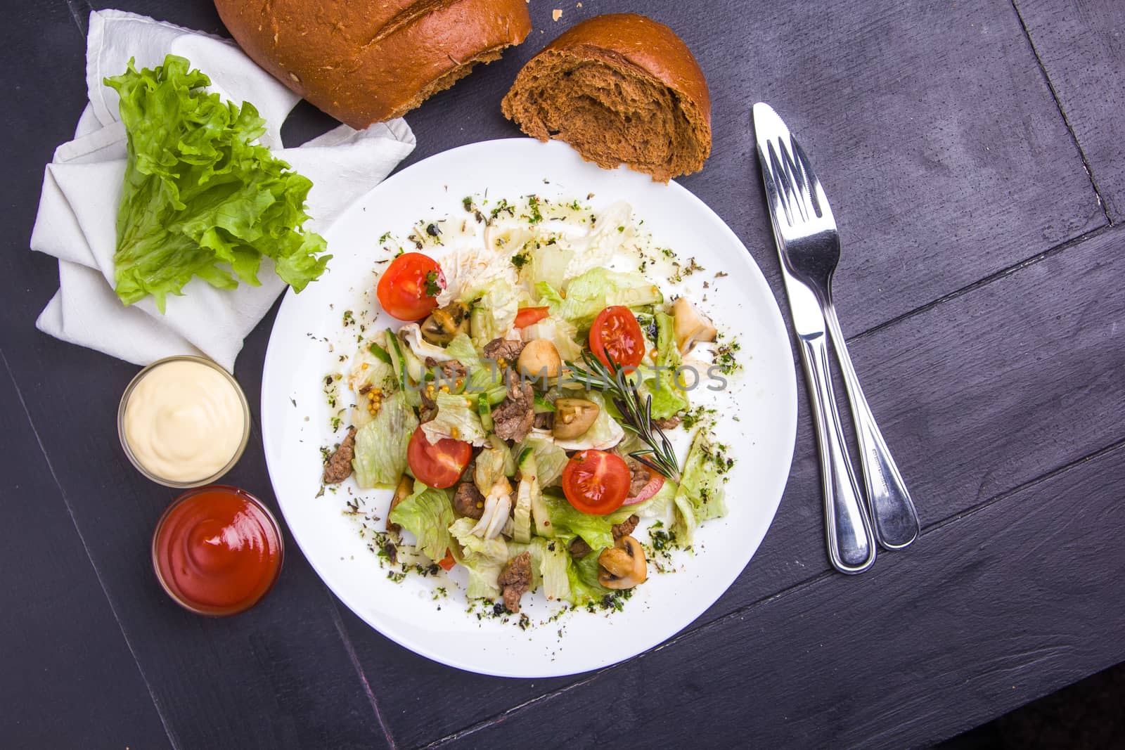 Concept: healthy food. Homemade salad with beef mushrooms and vegetables on white plate with ingredients bread and cutlery around