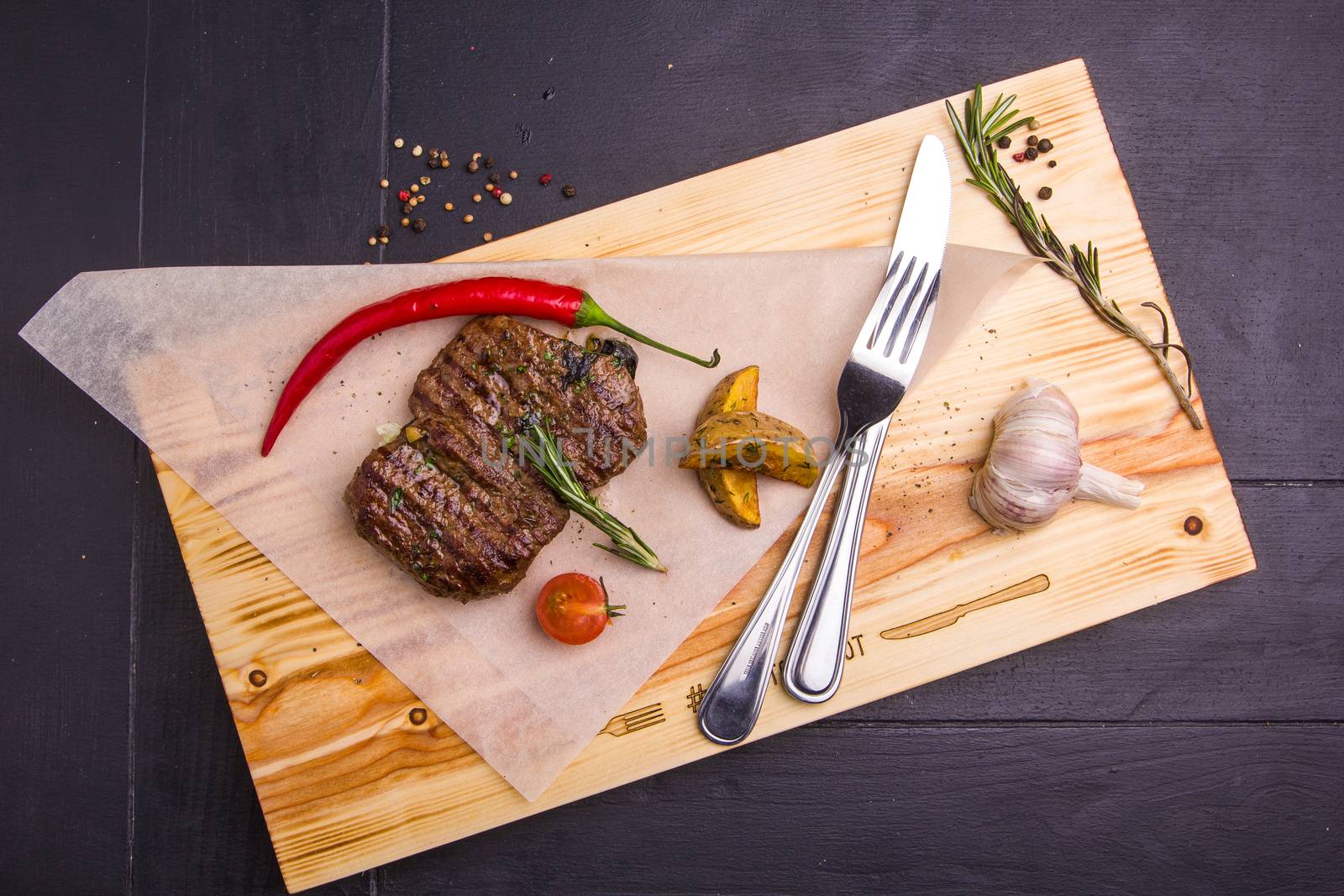 Concept: healthy food. Homemade grilled veal steak and vegetables on a wooden board with ingredients and cutlery around