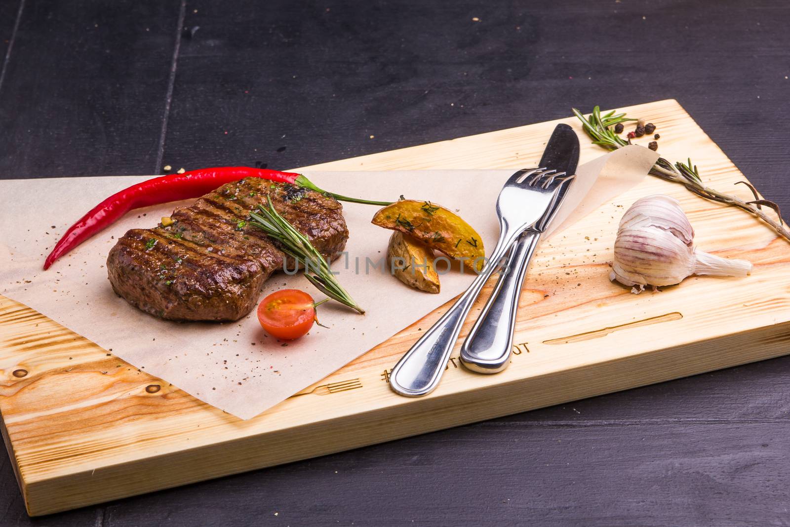 Concept: healthy food. Homemade grilled veal steak and vegetables on a wooden board with ingredients and cutlery around