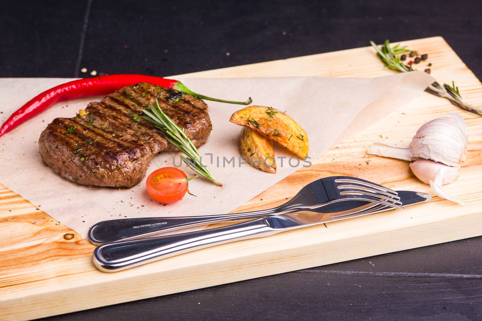 Concept: healthy food. Homemade grilled veal steak and vegetables on a wooden board with ingredients and cutlery around