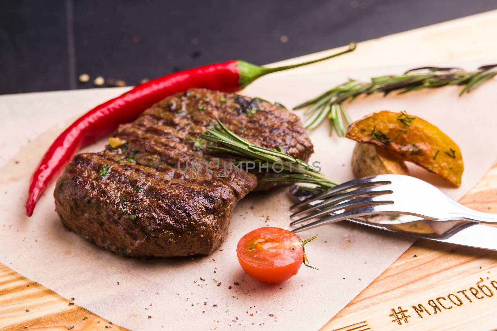 Concept: healthy food. Homemade grilled veal steak and vegetables on a wooden board with ingredients and cutlery around