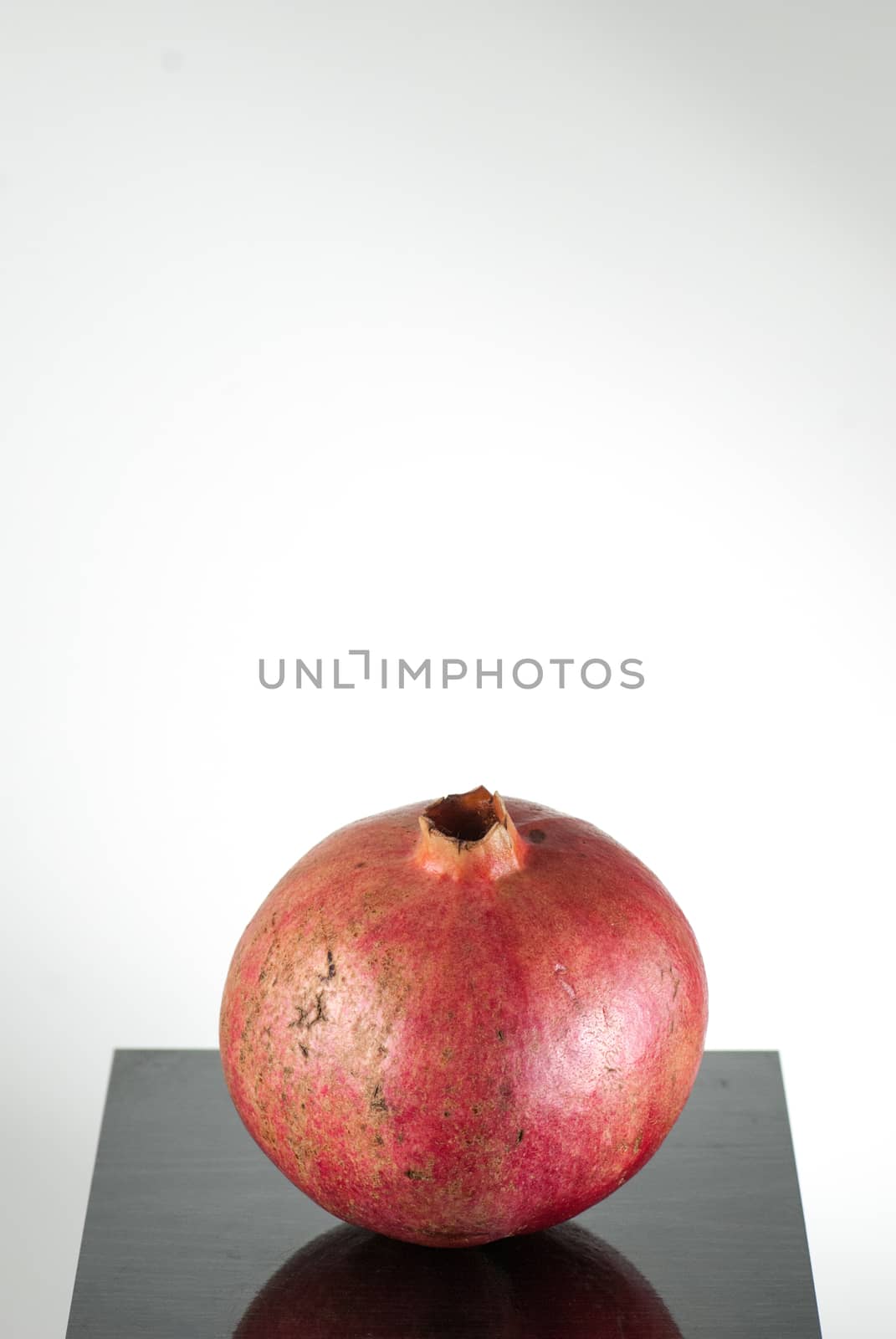  half ripe pomegranate fruit isolated on black wooden plane and white background. With copyspace
