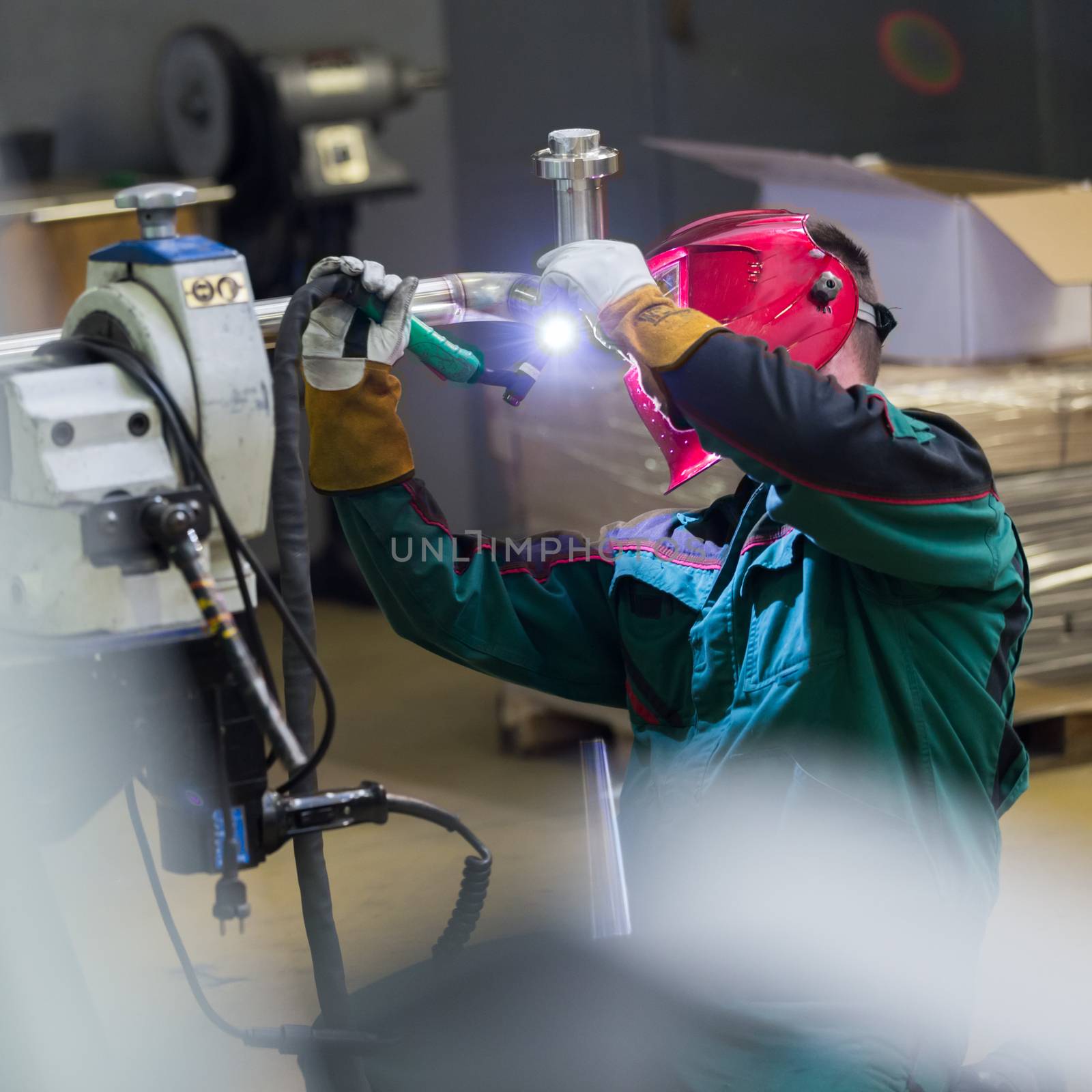 Industrial worker with protective mask welding inox elements in steel structures manufacture workshop. Square composition.