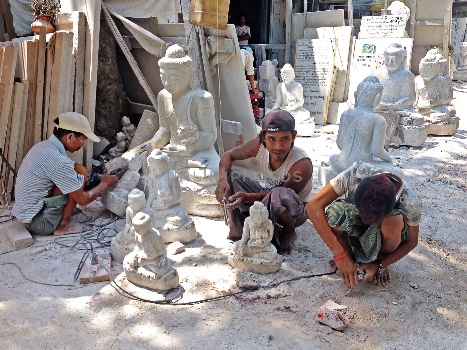 MANDALAY, MYANMAR, APRIL 20, 2013 : Burmese men are carving traditional marble Buddha statues, sitting in a street of Mandalay, Myanmar (Burma).