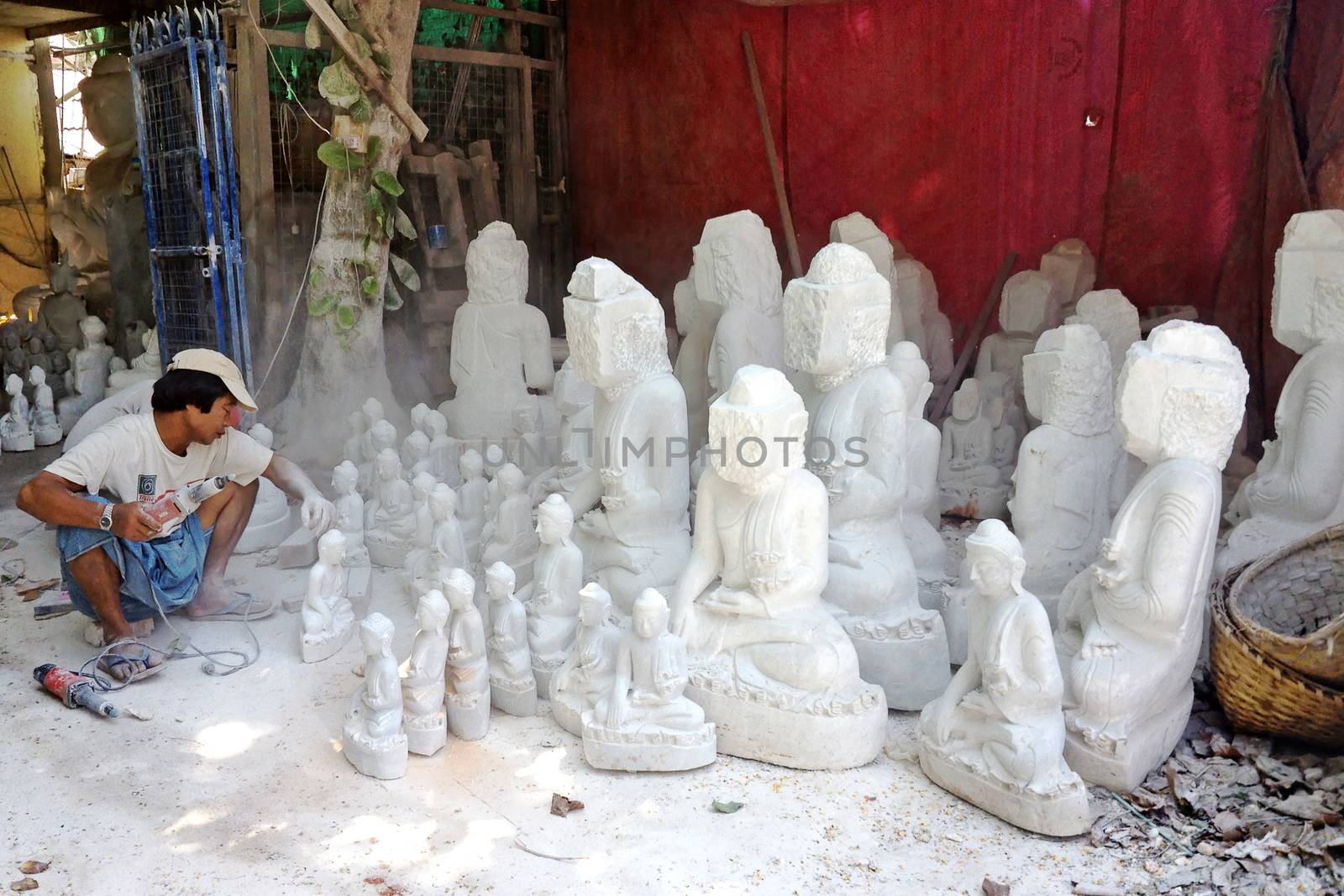 MANDALAY, MYANMAR, APRIL 20, 2013 : Burmese man are carving traditional marble Buddha statues, sitting in a street of Mandalay, Myanmar (Burma).