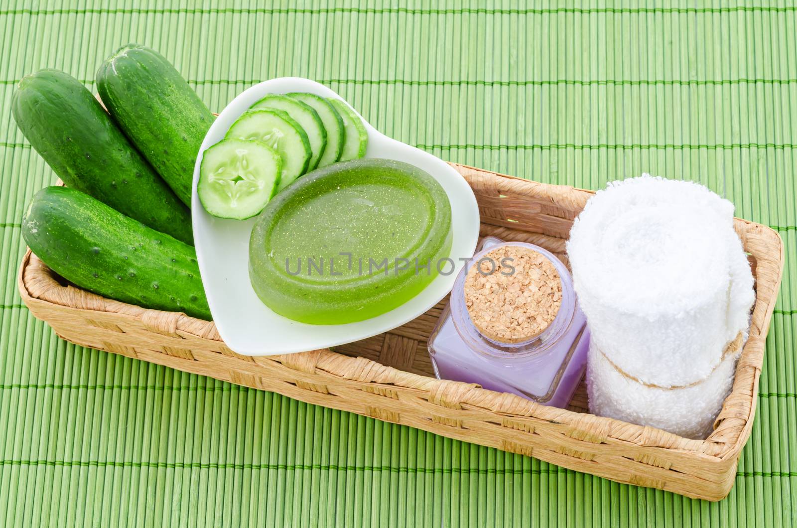 shampoo bottle with cucumber and towel in weave basket on green bamboo mat.