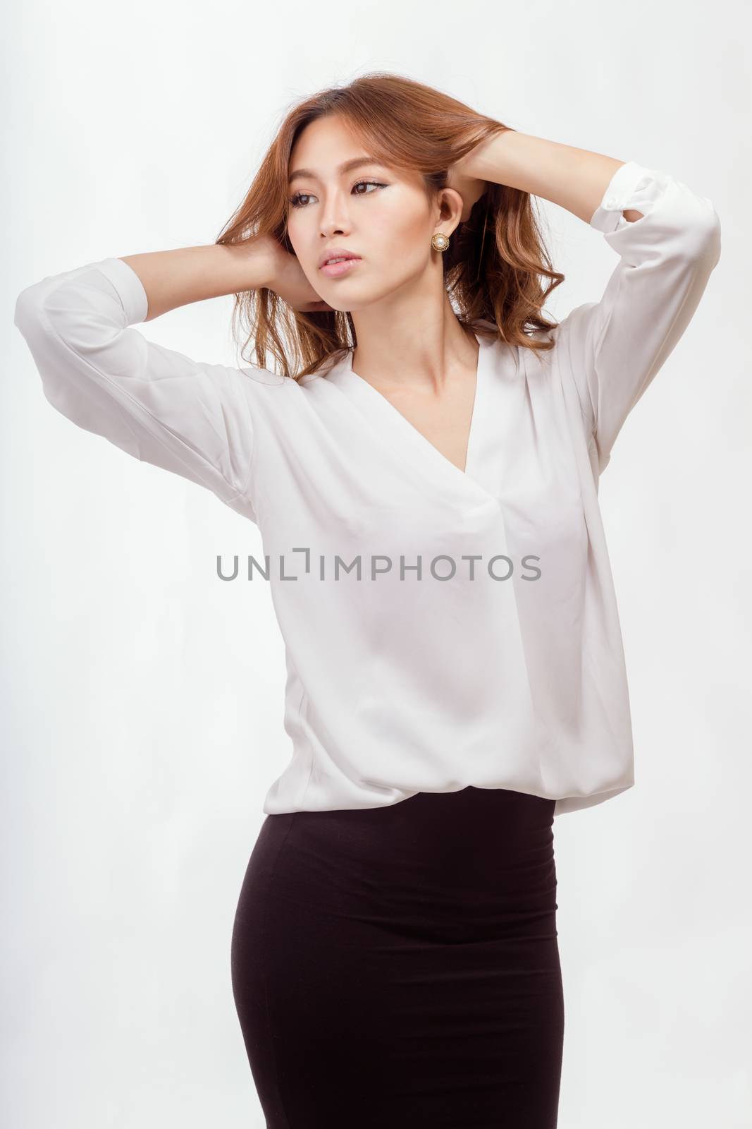 Attractive Asian American businesswoman in white blouse and black skirt with hands in hair
