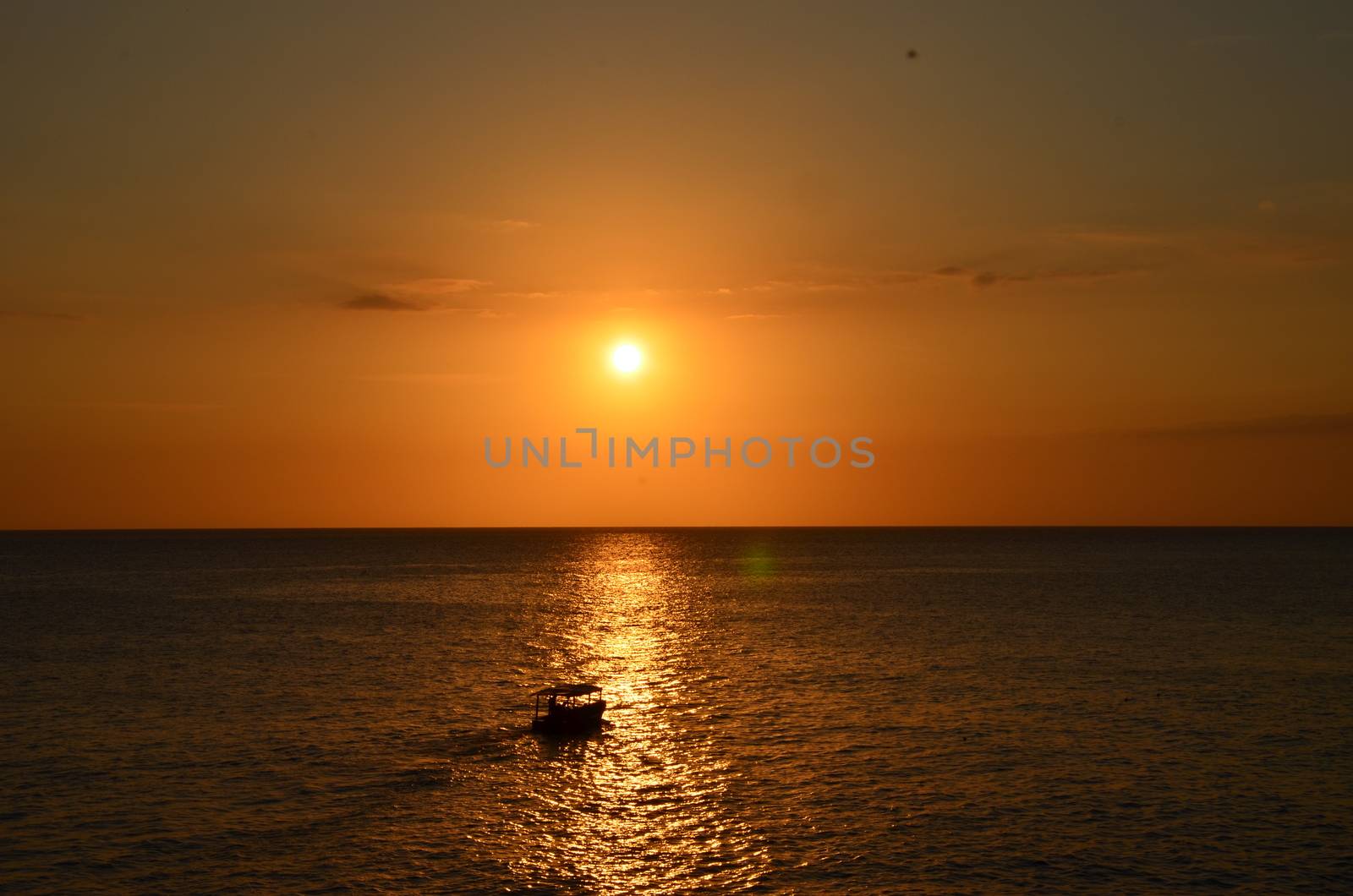 Sunset over the water in Jamaica. A boat is crossing in front of the setting sun.